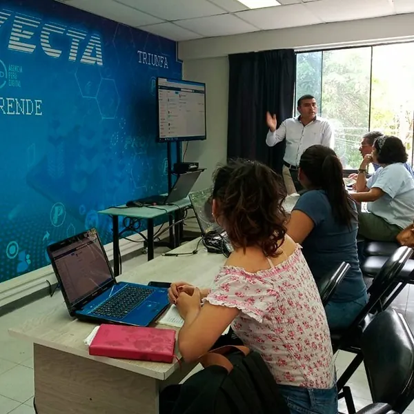 Leoncio Vilchez, con camisa blanca, enseñando frente a participantes junto a la pared azul de Proyecta